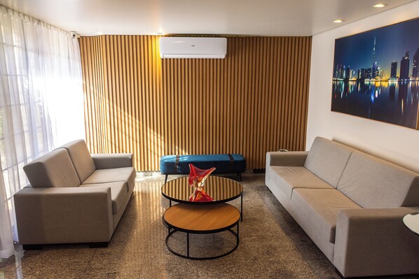 Una habitación de hotel moderna con sofá, una mesita redonda y un otoman azul.