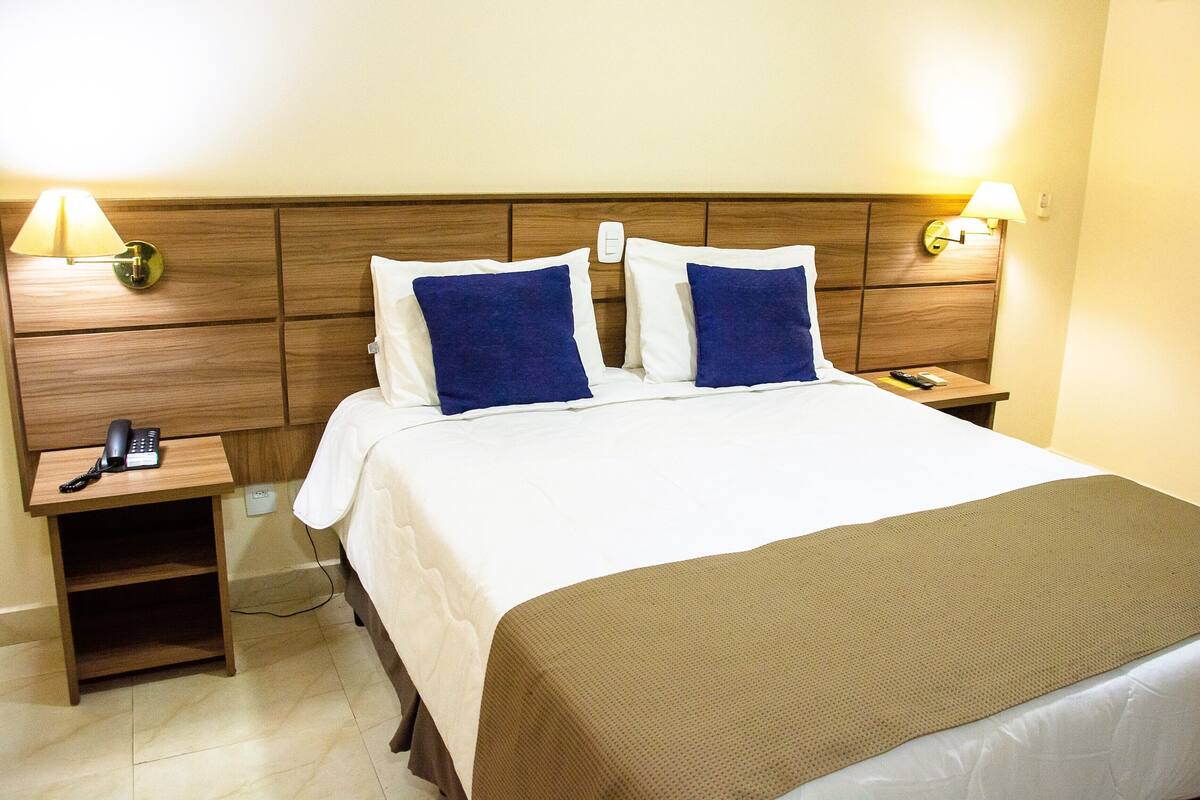 Habitación de hotel con una cama, dos lámparas de noche, un teléfono junto a la cama y una mesita de noche.