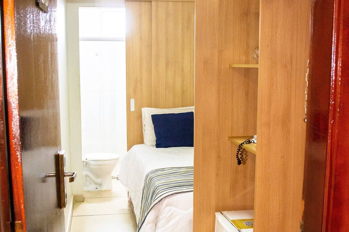 Habitación de hotel compacta con cama, un refrigerador pequeño y un armario de madera.