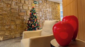 Un muro de piedra, un árbol de Navidad, un jarrón rojo y un sillón color beige.