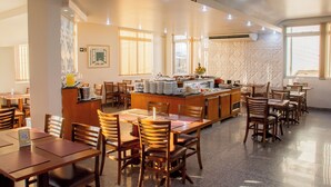 Un comedor amplio con varias mesas y sillas de madera, un mostrador de buffet central y grandes ventanales que permiten la entrada de luz natural.