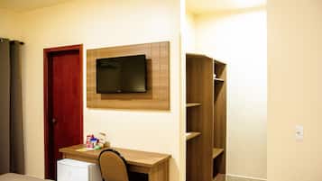 Ein Zimmer mit einem Holztisch, einem an der Wand montierten Fernseher, einer roten Tür und einem kleinen weißen Kühlschrank.