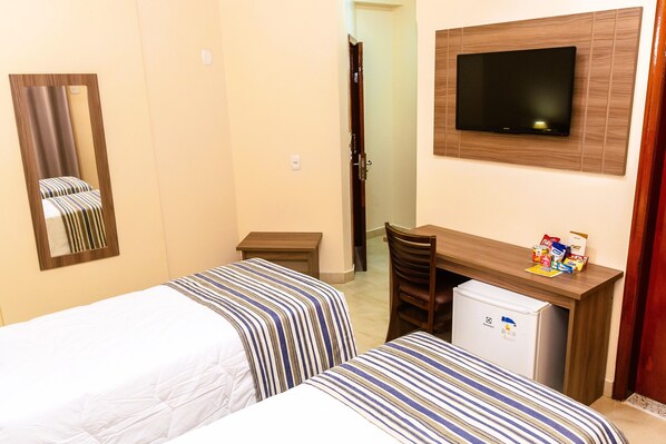 Habitación de hotel con dos camas, televisión, escritorio con refrigerador y espejo.