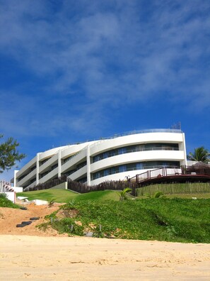 Um edifício moderno de vários andares com fachada curva, telhado plano e área ajardinada com grama e plantas na frente.