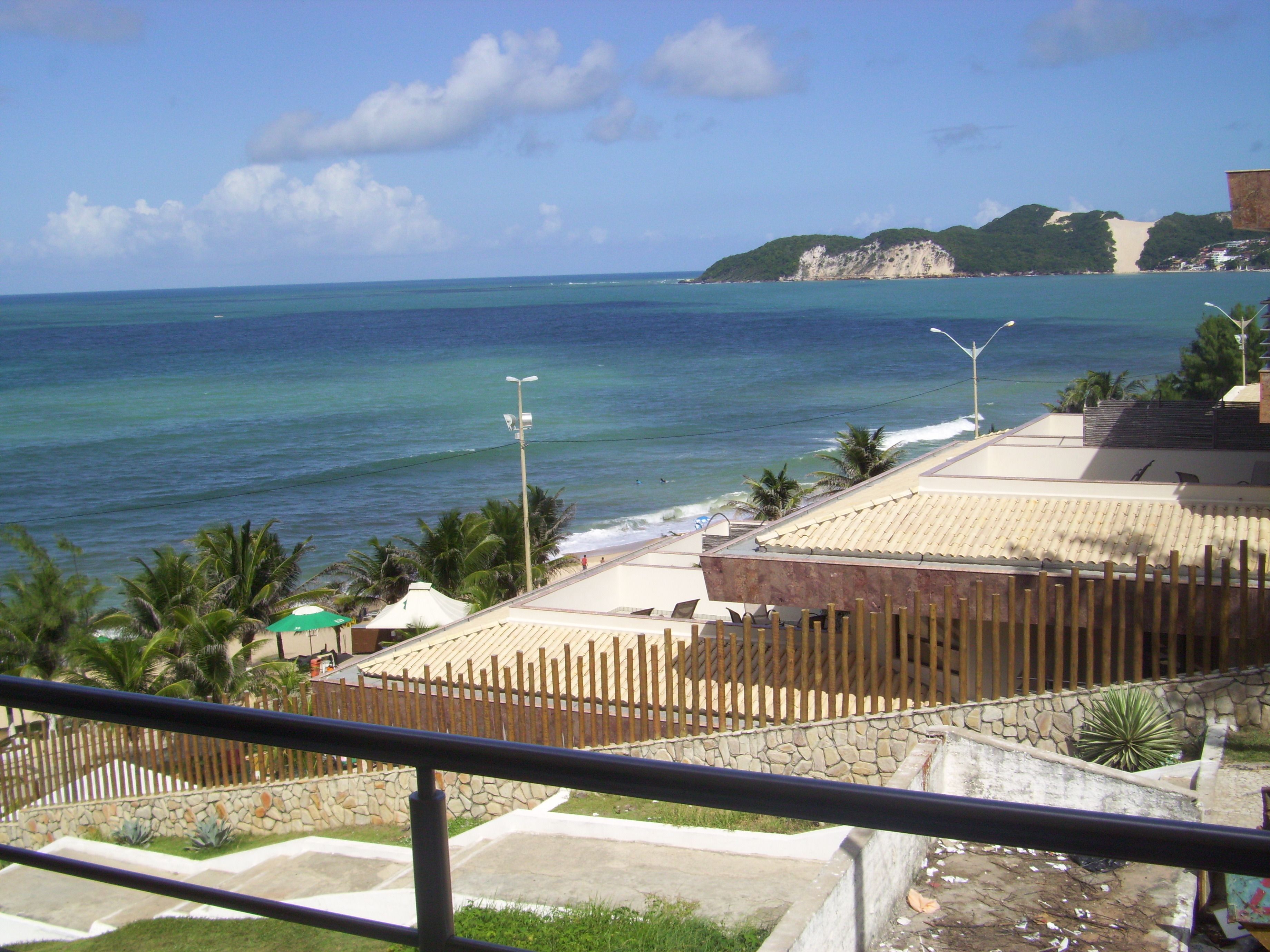 A coastal view with a clear sky, a sandy beach, and a rocky cliff in the distance.