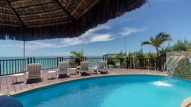 A pool area with a thatched roof, lounge chairs, and a view of the ocean. - Apart Hotel Vespucci Residence (Natal)