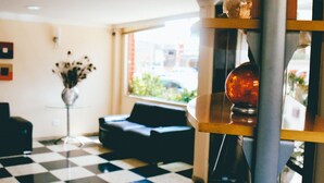 A checkered floor, a black sofa, a glass table with a vase of flowers, and a window with a view of the outside. - Hotel Pedra Negra (Governador Valadares)