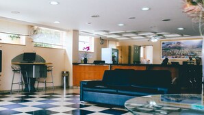 A lobby with a checkered floor, a reception desk, a sofa, and a glass table. - Hotel Pedra Negra (Governador Valadares)