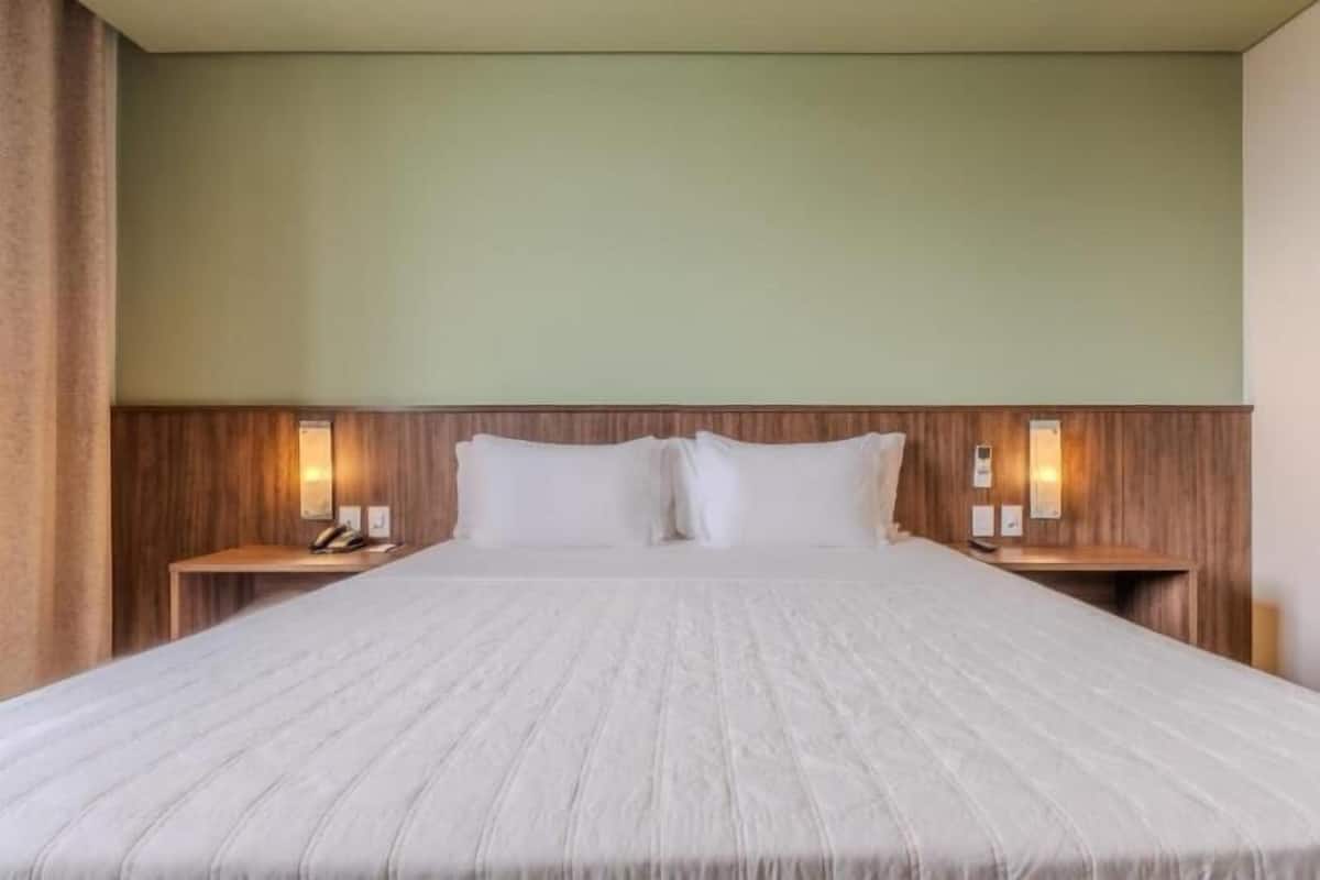 A hotel room with a large bed, wooden headboard, two bedside tables with lamps, and a green wall.