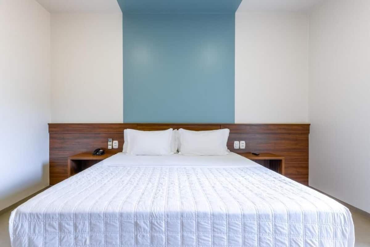 A hotel room with a large bed, wooden headboard, white bedding, and a blue accent wall.