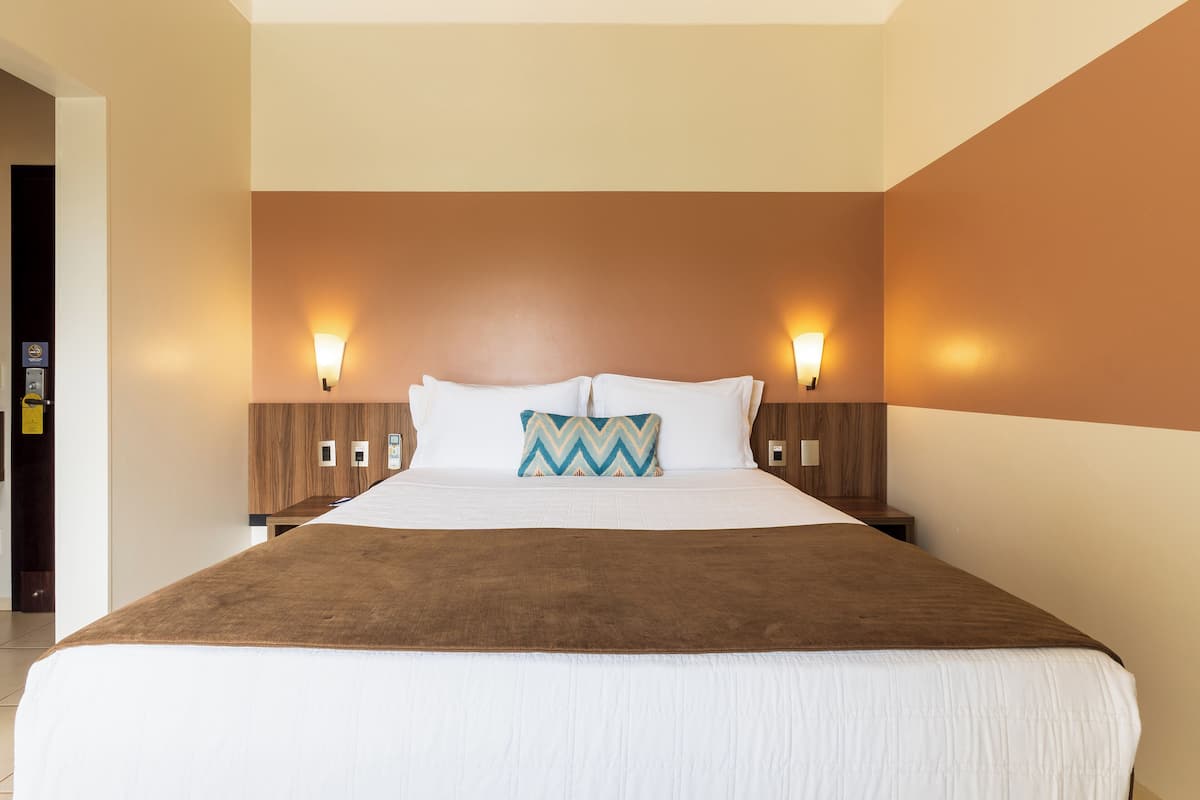 A hotel room with a large bed, two bedside tables, and wall-mounted lamps.