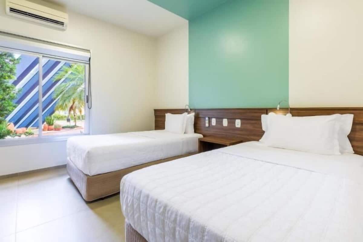 A hotel room with two beds, a large window with a view of palm trees, and a wooden headboard.