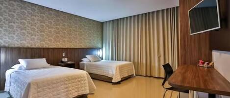 Habitación de hotel con dos camas, un escritorio, un televisor y una ventana con cortinas.