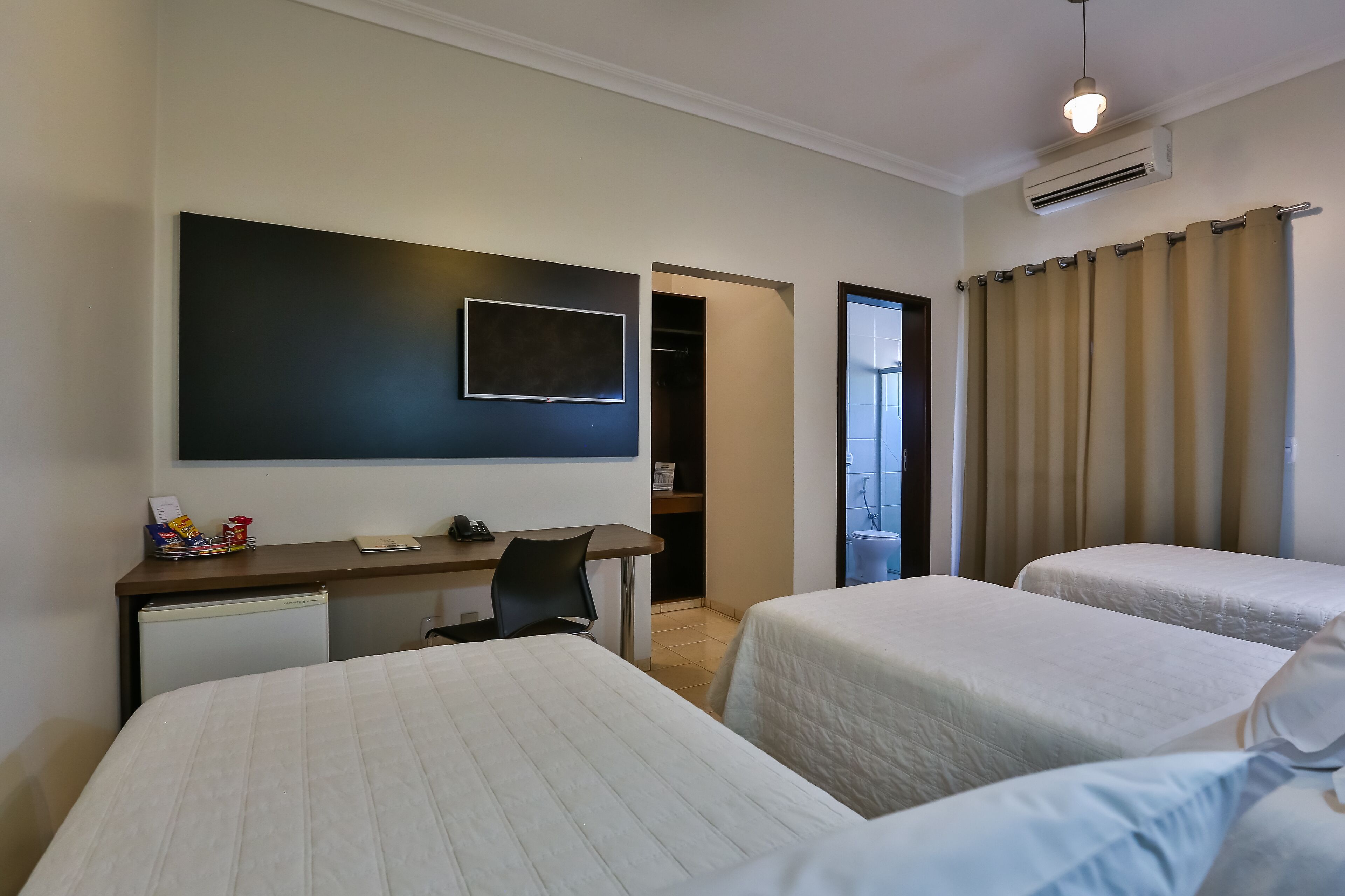 Una habitación de hotel con dos camas, un escritorio, una silla, un televisor y un armario.