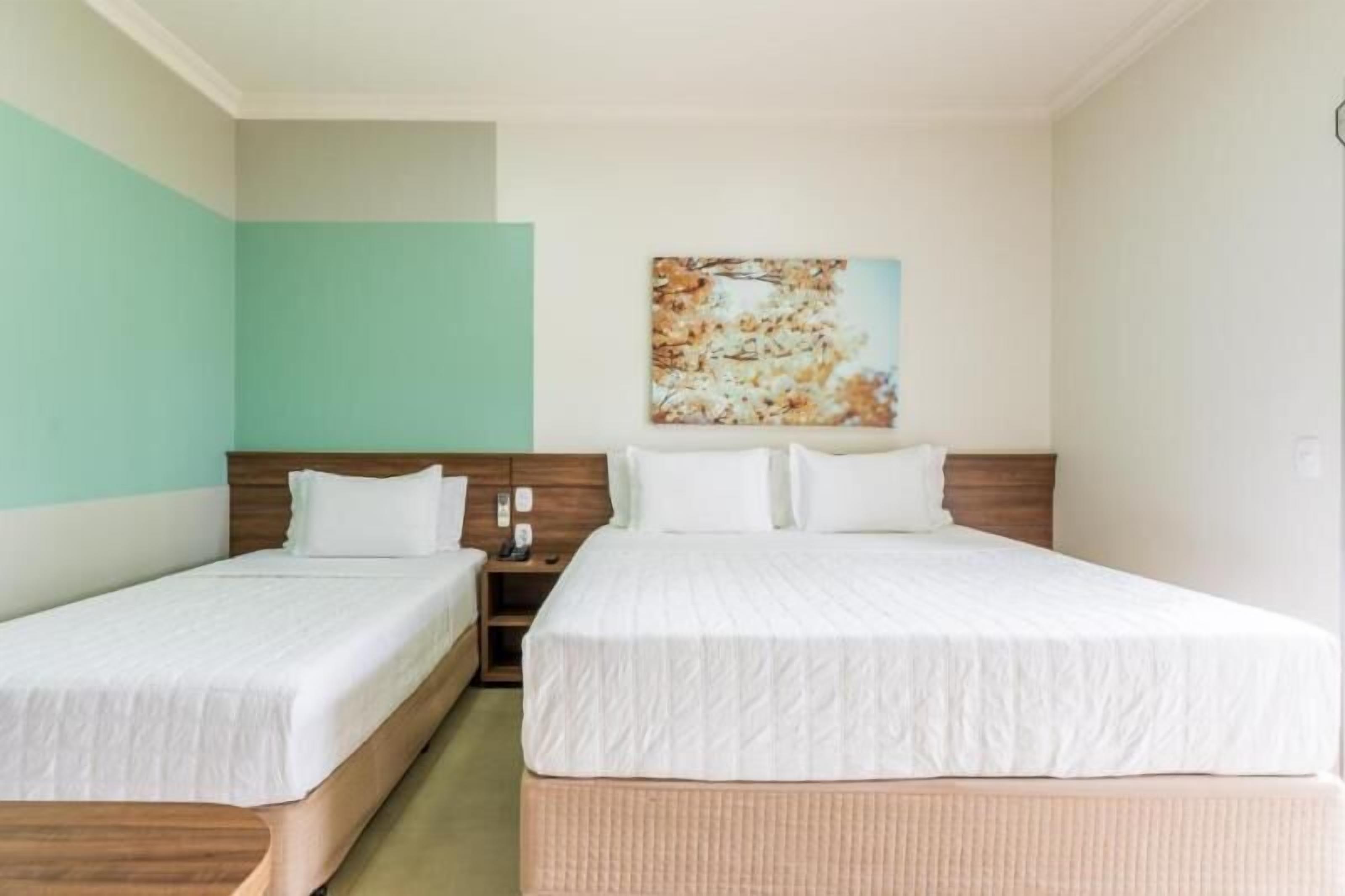 A hotel room with two single beds, a wooden headboard, a nightstand, and a painting on the wall.