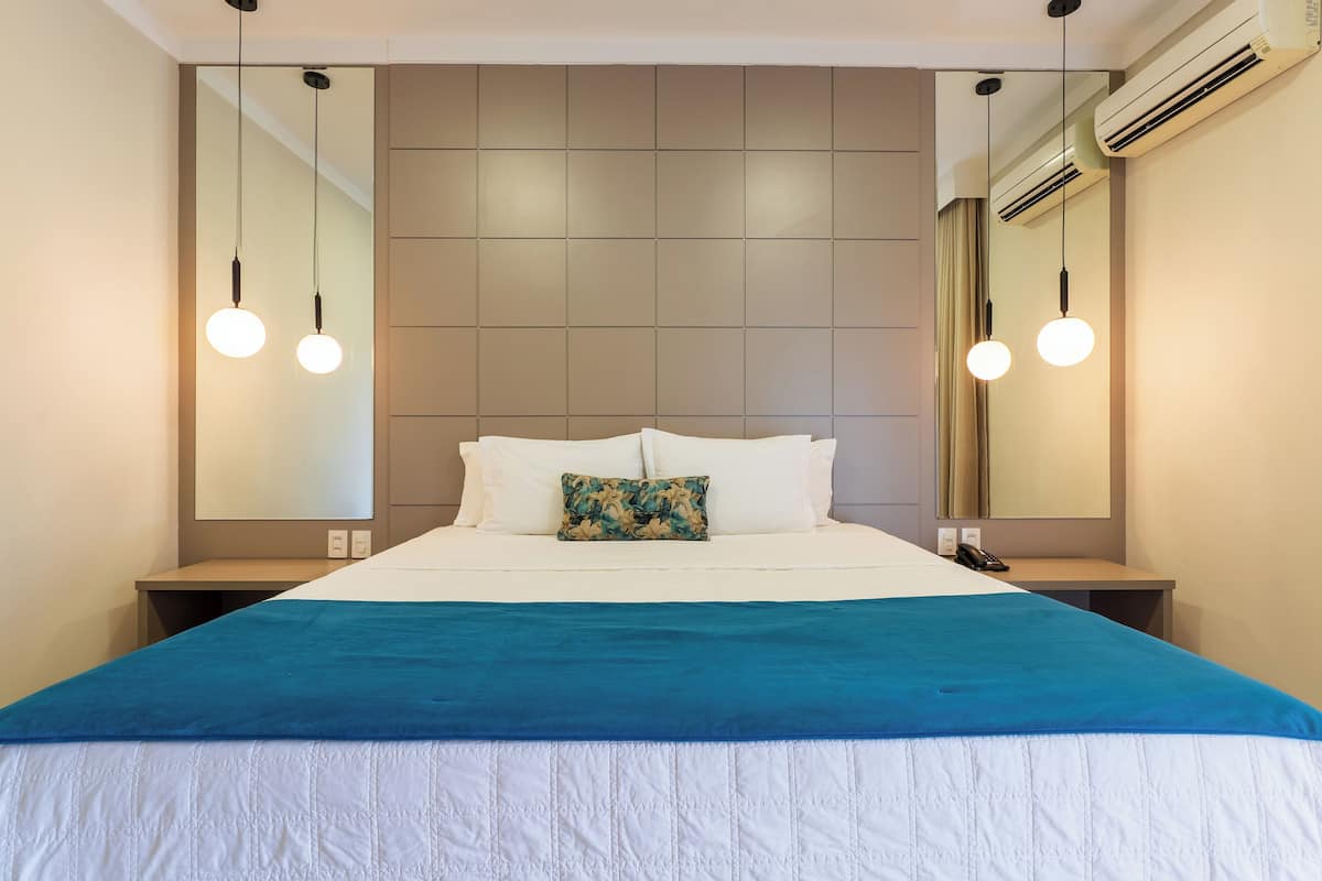 A neatly made bed with a blue and white bedspread, two bedside tables with lamps, a mirror, and an air conditioning unit.