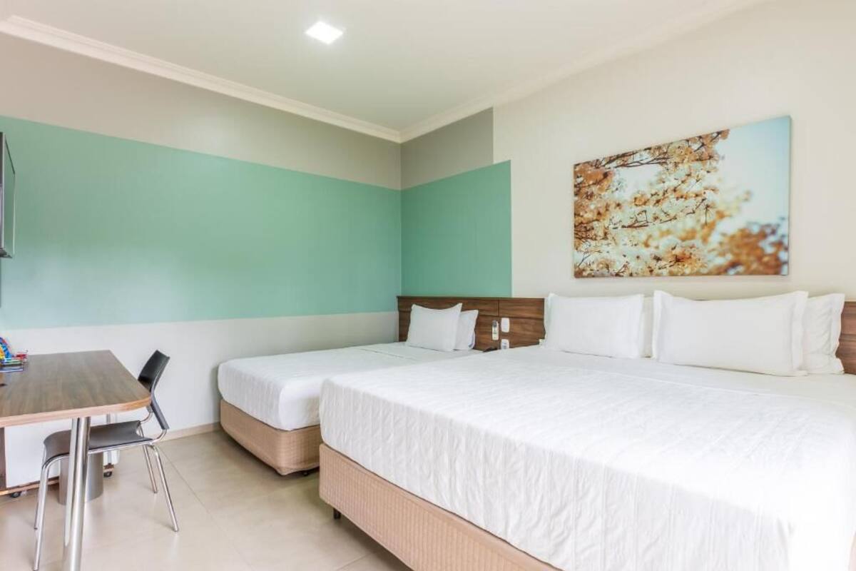 A hotel room with two beds, a wooden desk, and a painting on the wall.