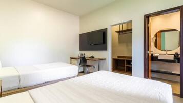 Habitación de hotel con dos camas individuales, un escritorio con silla, un televisor de pantalla plana montado en la pared, un espejo y un armario de madera.