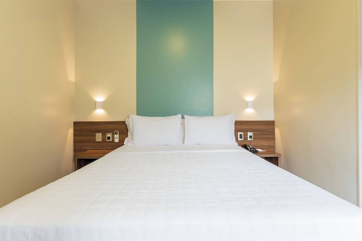 A hotel room with a large bed, two bedside tables, and a wall-mounted light fixture.