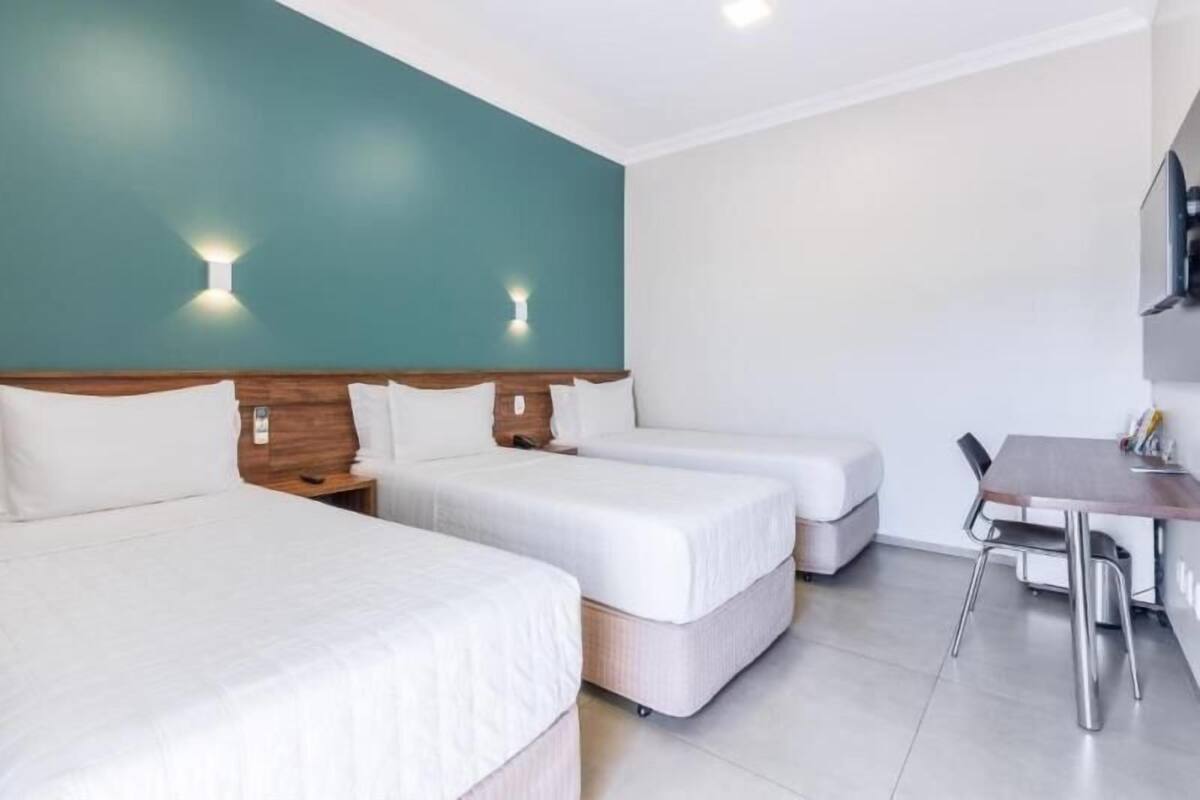 A hotel room with two single beds, a wooden headboard, a small table with chairs, and a TV mounted on the wall.