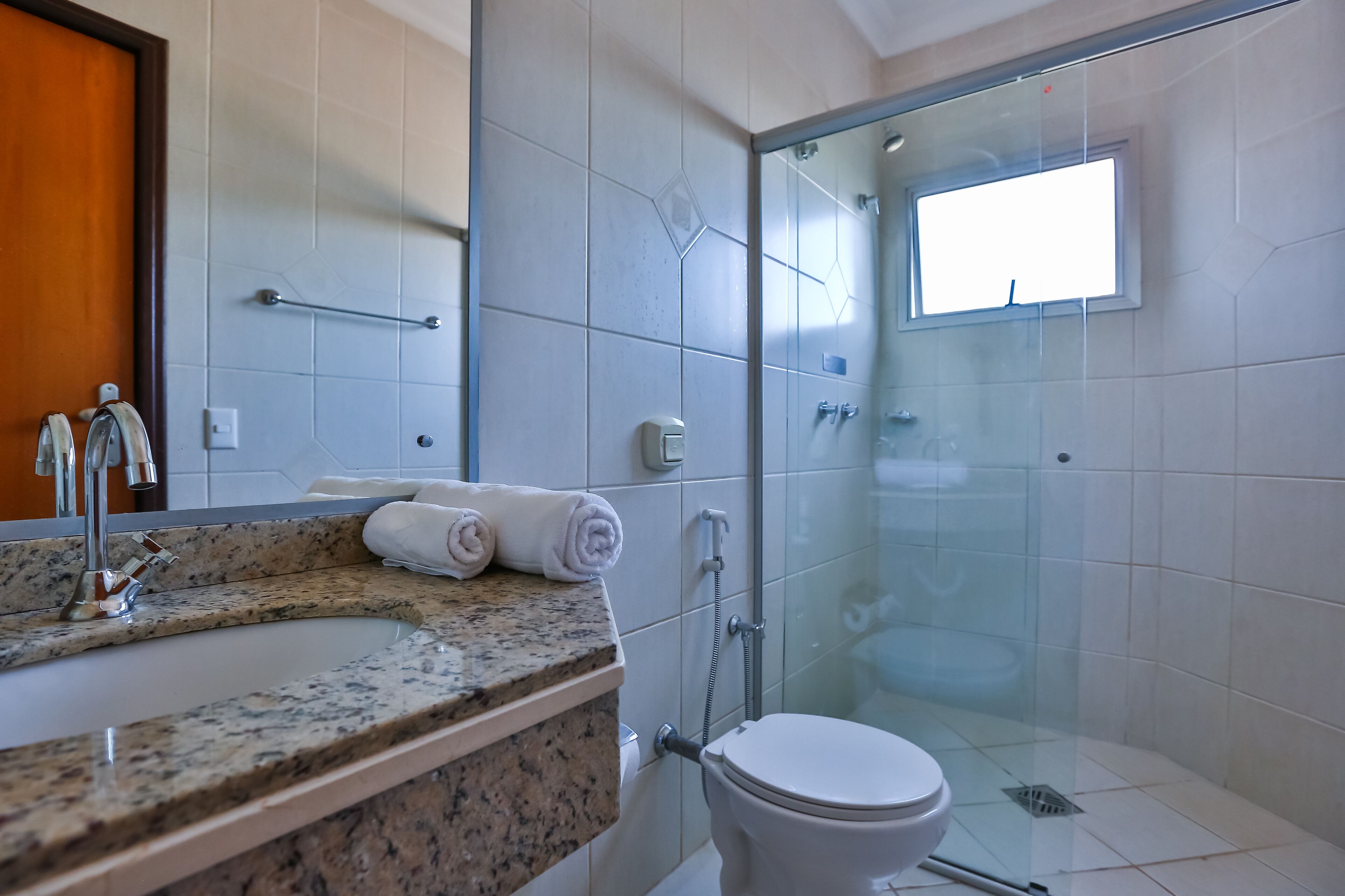A modern bathroom with a granite countertop, a glass shower enclosure, and a white toilet.