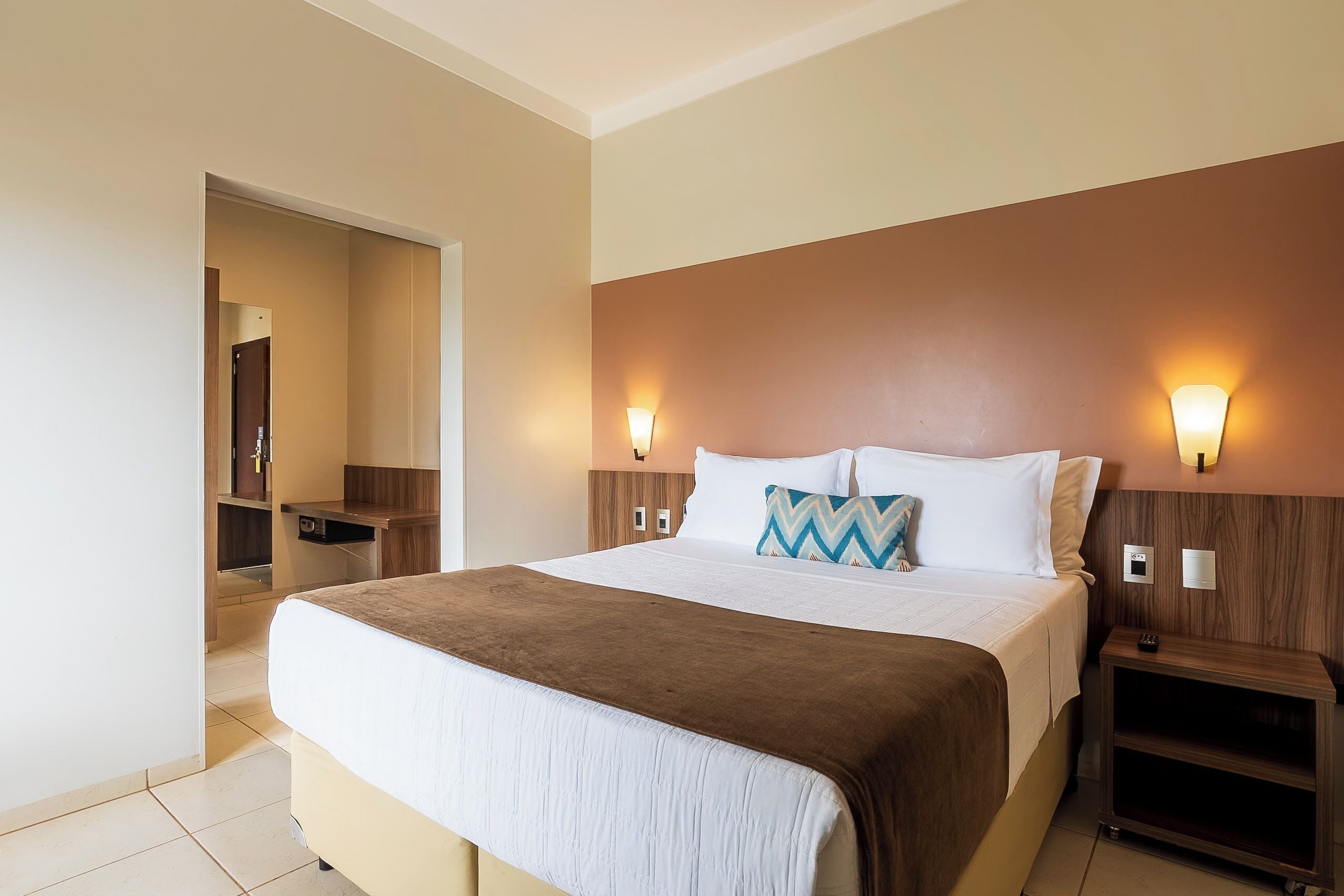 A hotel room with a large bed, bedside tables, a wardrobe, and a mirror.