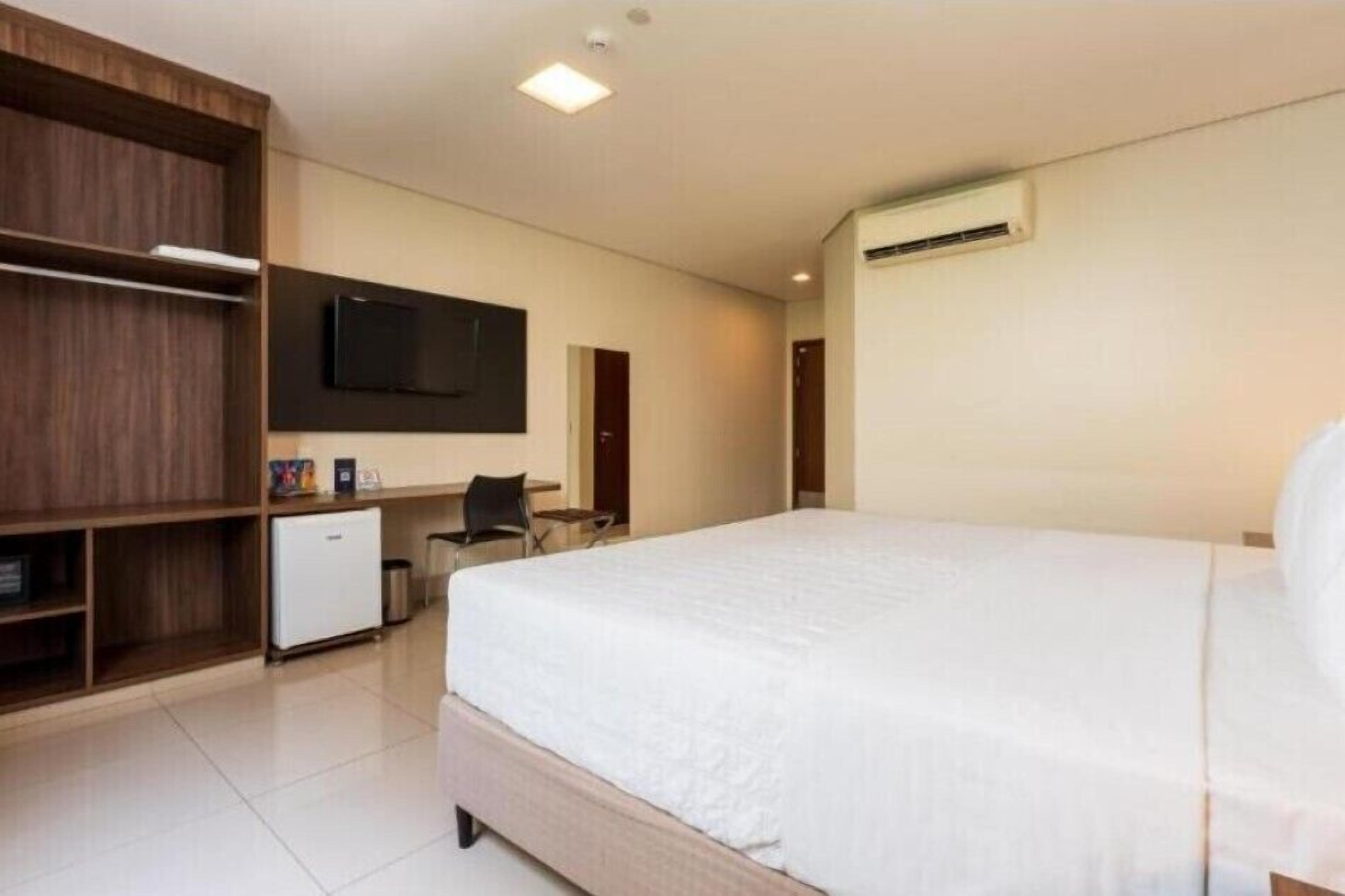 Una habitación de hotel moderna con una cama grande, un escritorio, un armario y un televisor de pantalla plana.