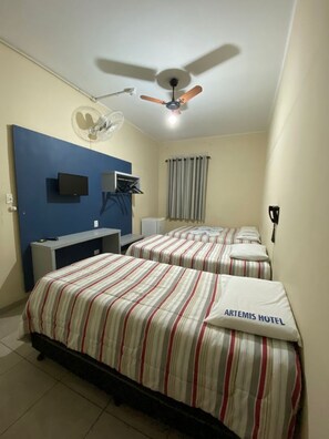 A hotel room with two beds, a desk, a ceiling fan, a TV, and a window with curtains. - Artemis Hotel (Sao Paulo)