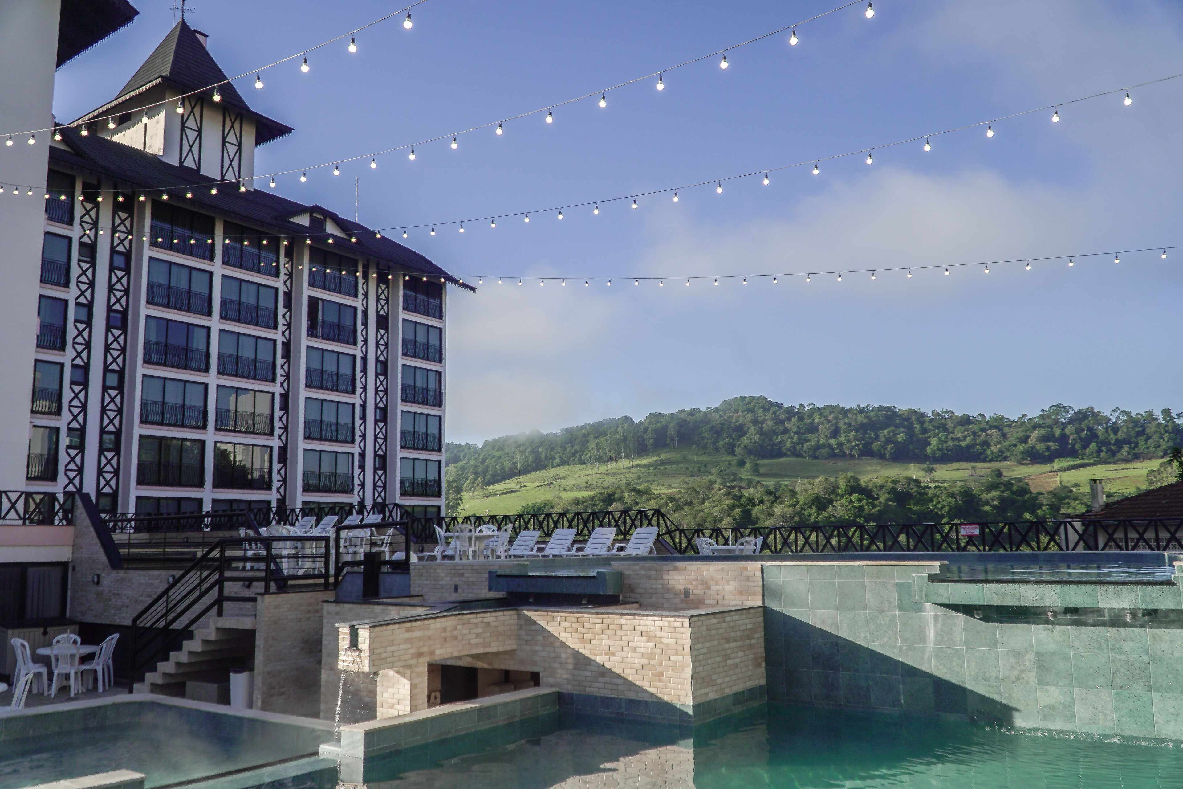 Un hotel con piscina, zona de estar al aire libre y luces colgantes.