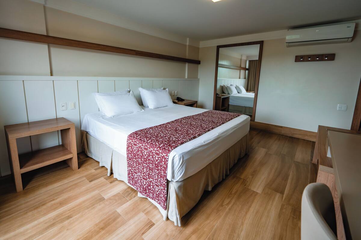 A bedroom with a large bed, bedside tables, a mirror, and an air conditioning unit.