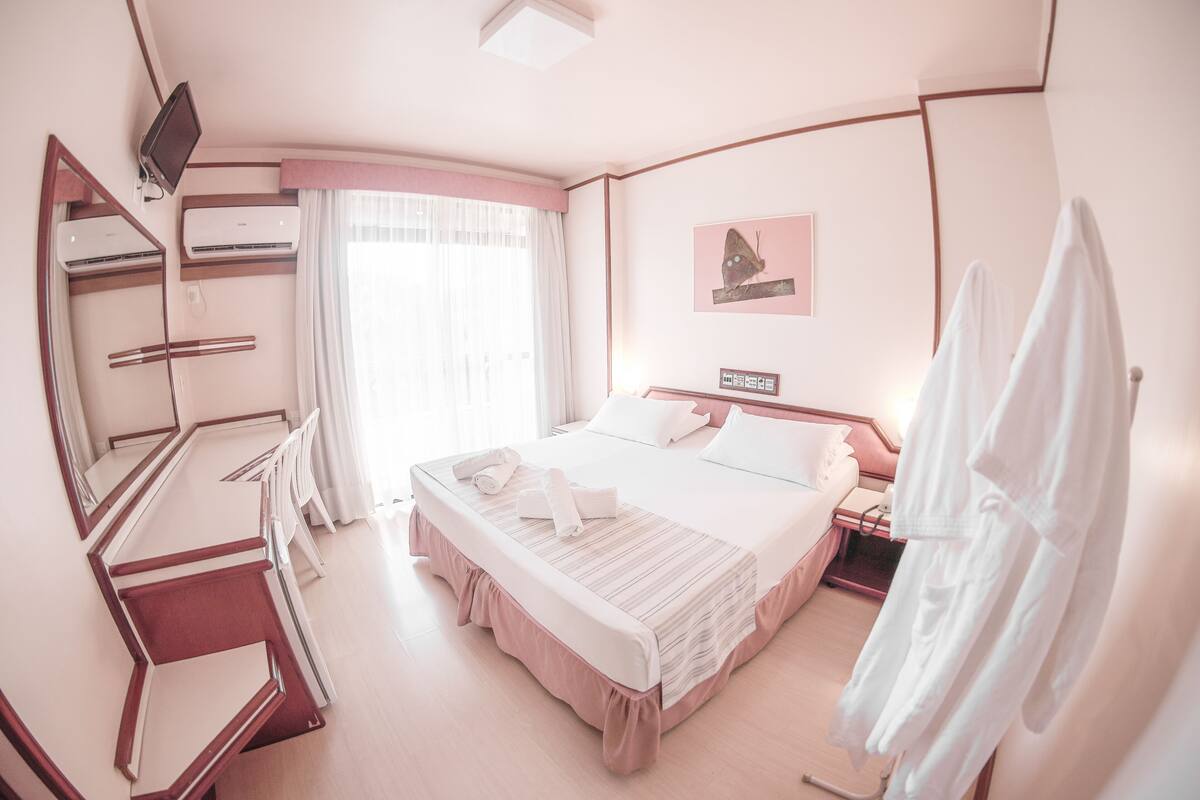 A hotel room with a large bed, a desk with a chair, a wardrobe, and a window with curtains.