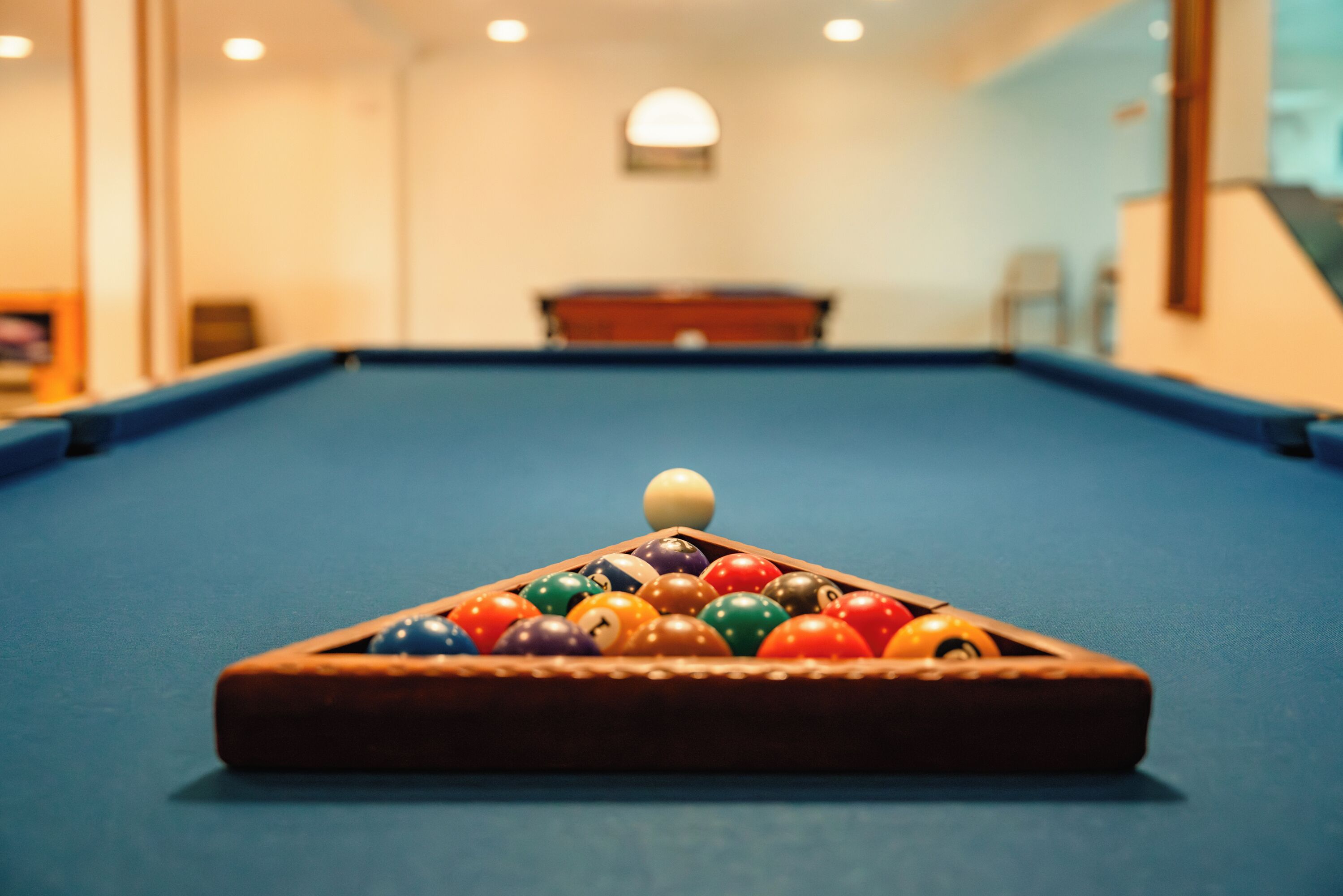 A pool table with a triangular rack of billiard balls in a room with a blue carpet and a wooden ceiling.
