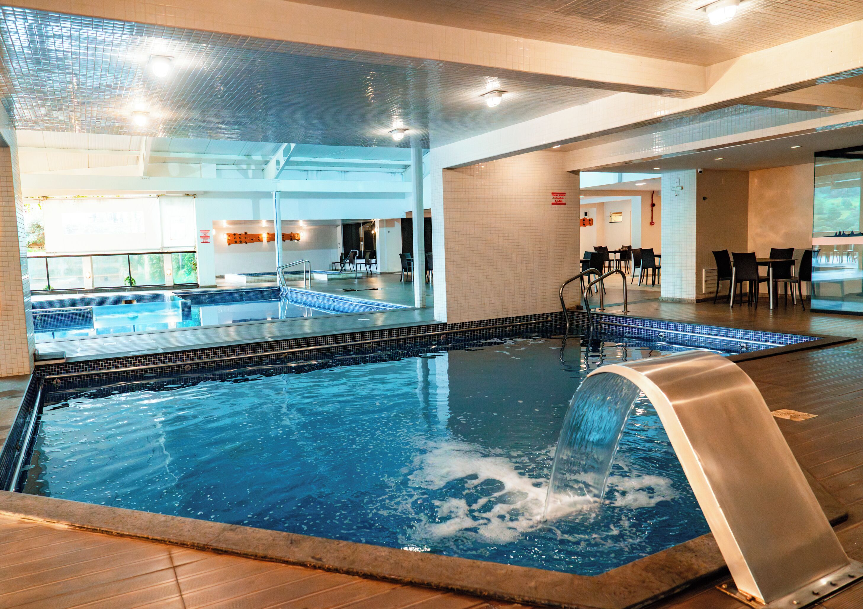 Une piscine intérieure à l’eau claire, dotée d’un plongeoir et d’un espace détente avec des tables et des chaises.