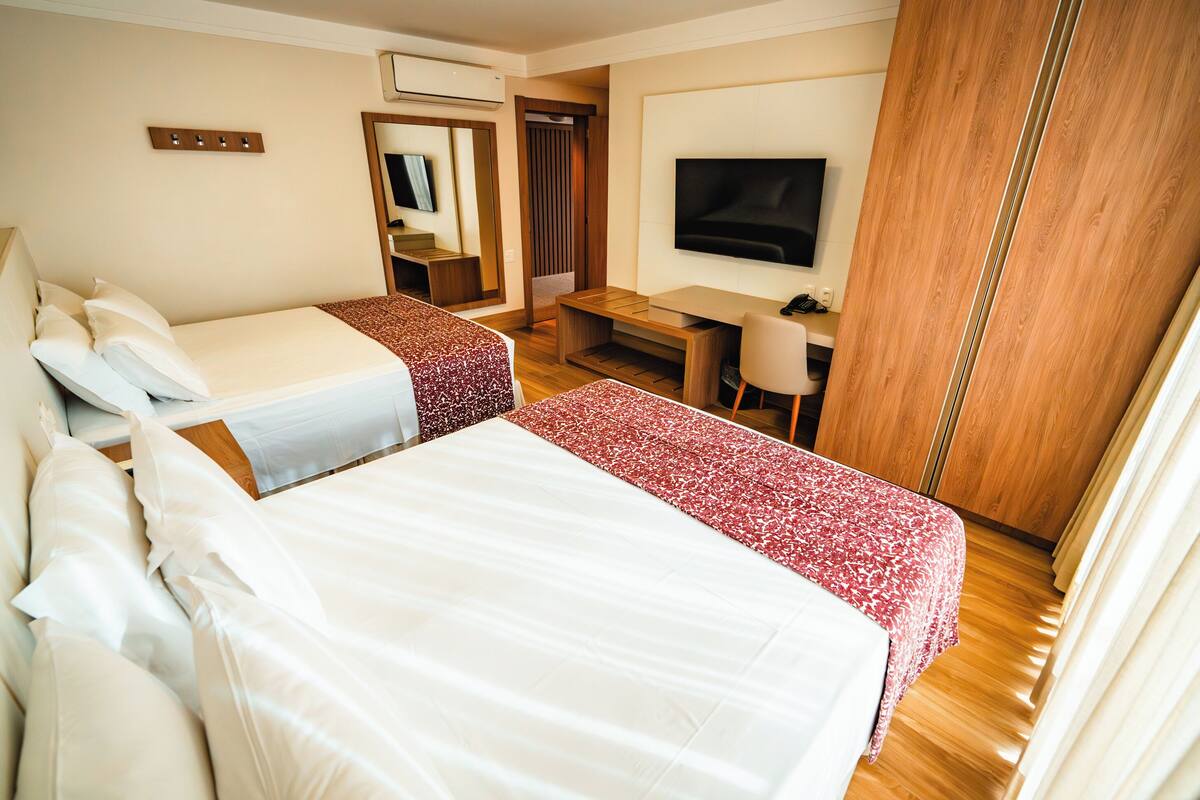 A hotel room with two beds, a desk, a TV, and a wardrobe.