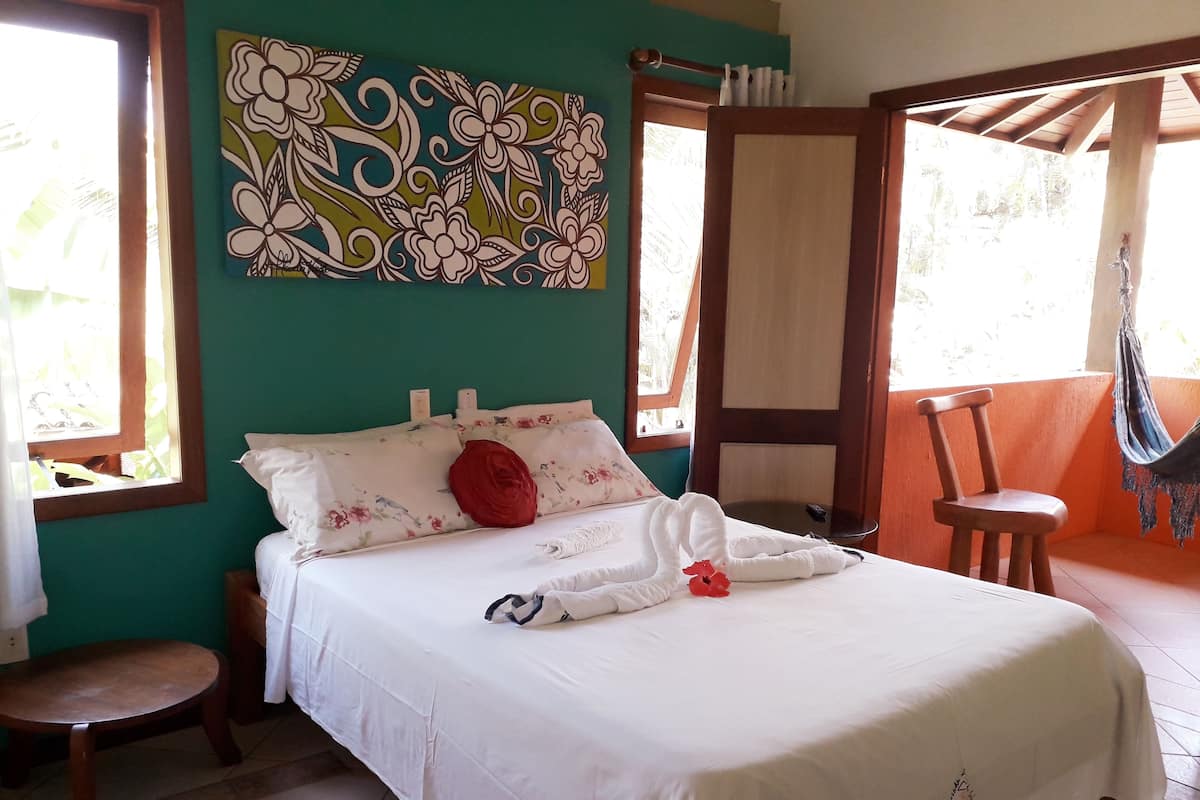 Quarto com cama, cadeira, rede e pintura na parede.