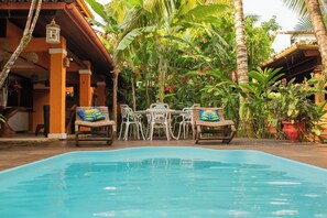 A pool area with lounge chairs and a table, surrounded by lush tropical plants and a wooden deck. - Pousada Villa do Sol (Itacaré)