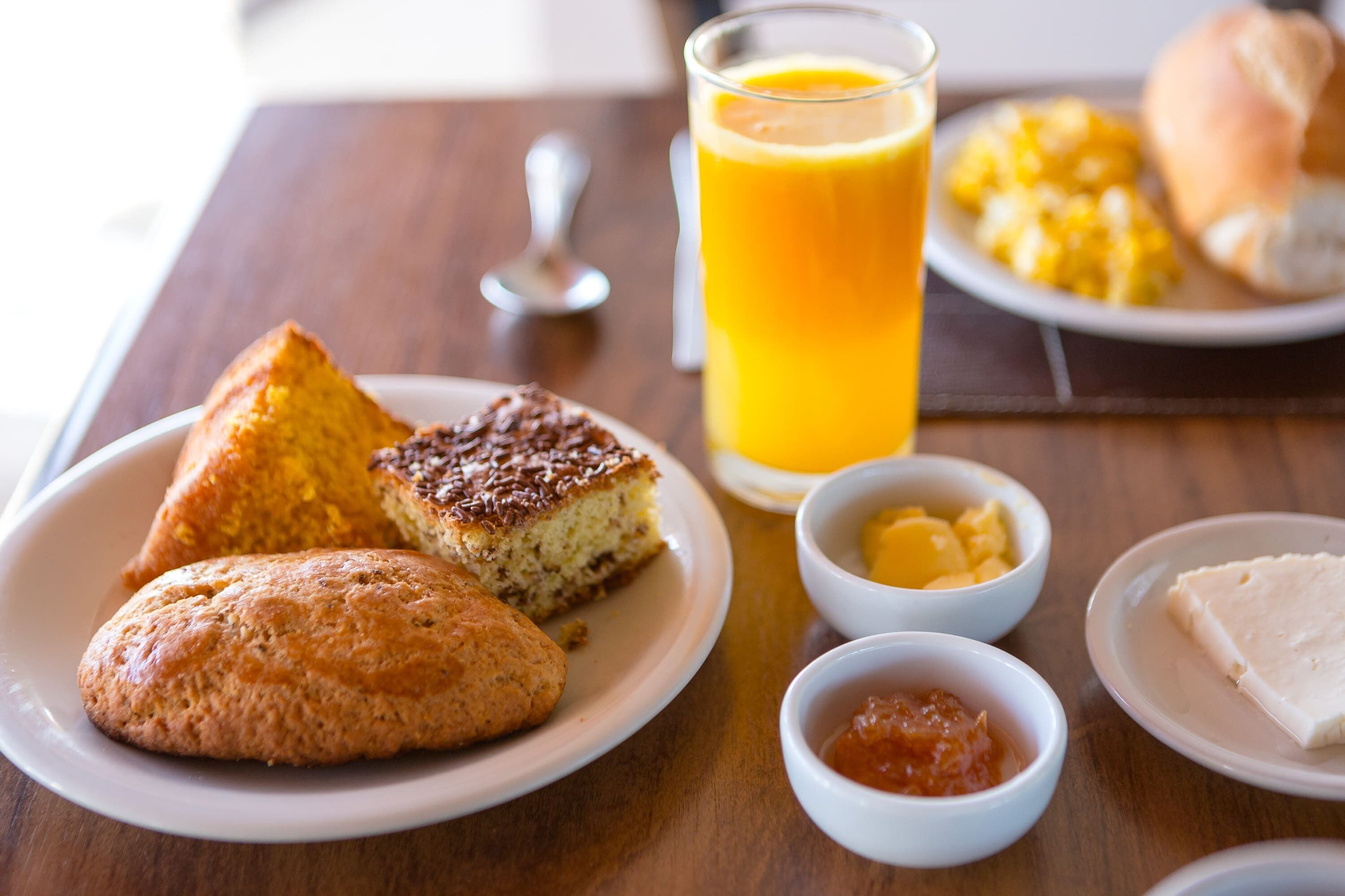 A breakfast setting with a plate of muffins, a glass of orange juice, and small bowls of butter and jam.