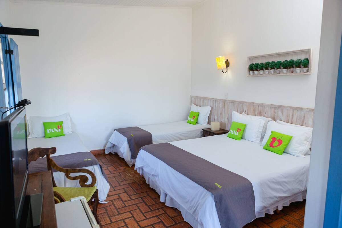 A hotel room with two beds, a wooden headboard, a shelf with potted plants, and a desk with a chair.