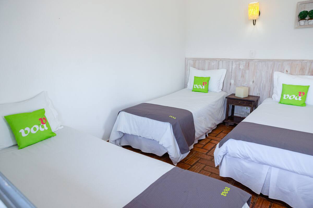 A hotel room with three beds, each with white bedding and green pillows with 'vod' branding.