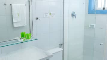Un baño moderno con cabina de ducha de vidrio, inodoro blanco y repisa de vidrio con artículos de aseo.