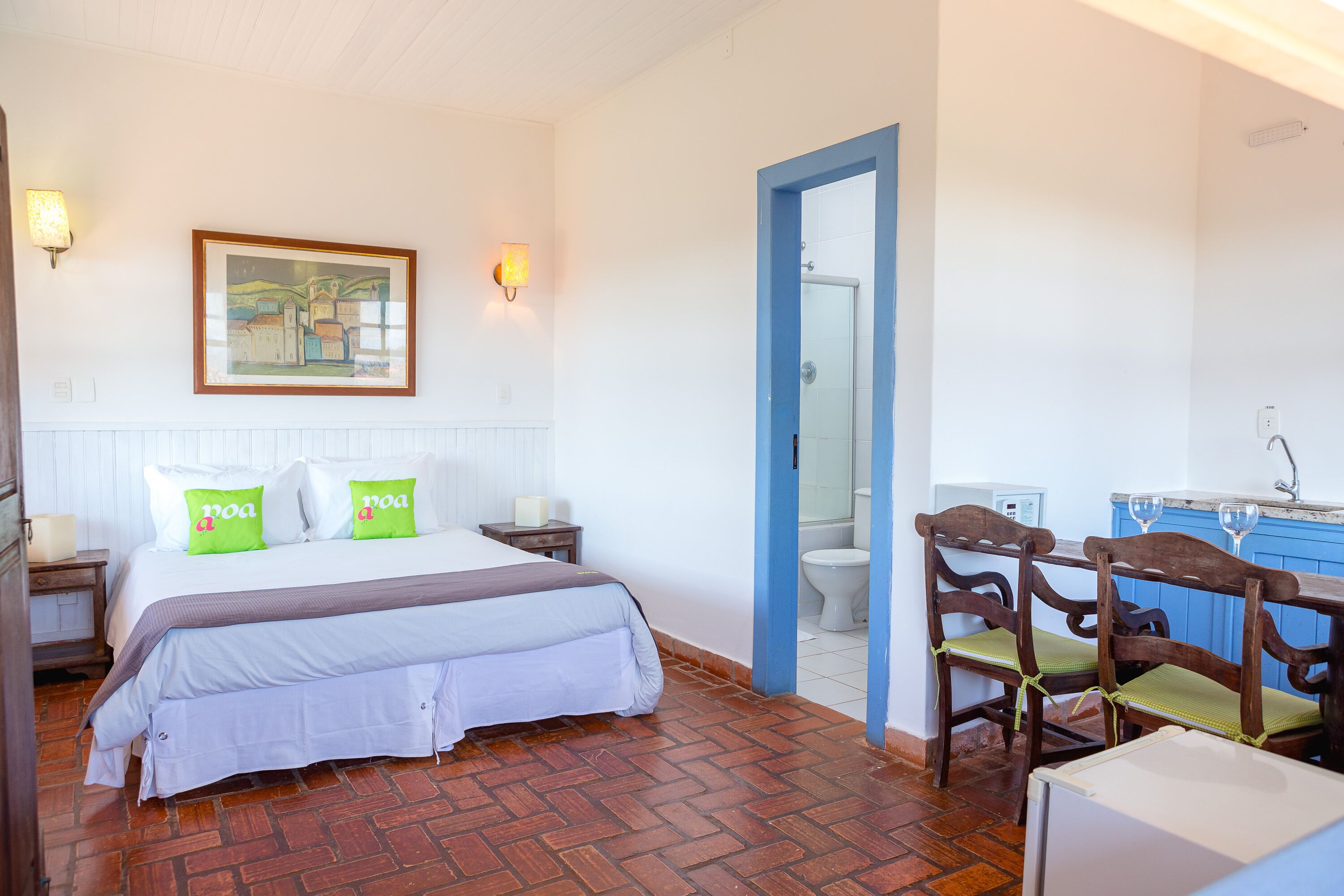 A bedroom with a bed, bedside tables, a painting, and a bathroom visible through an open door.