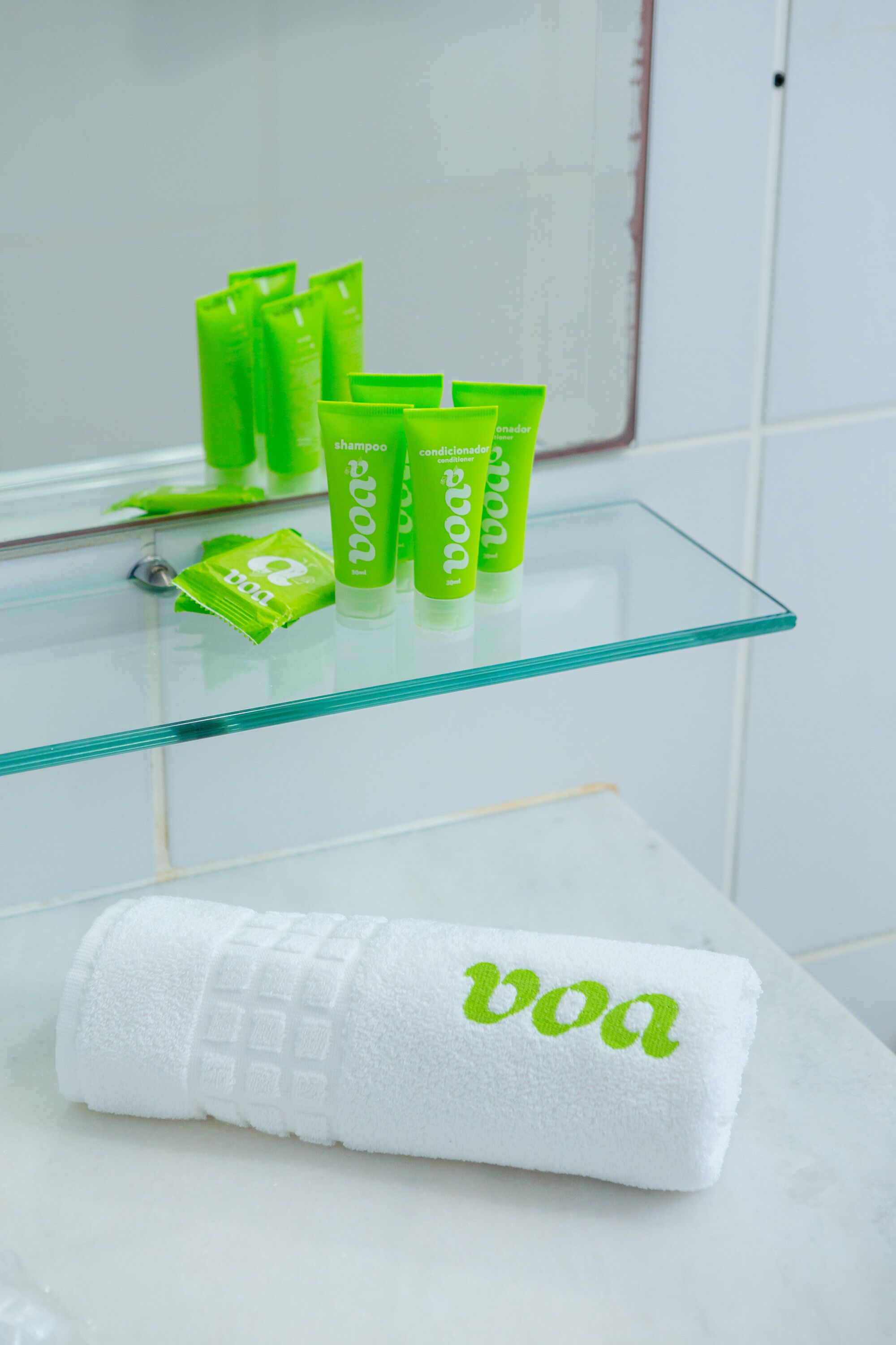 Un baño con un estante de vidrio que sostiene artículos de tocador verdes y una toalla blanca con la palabra 'boa'.