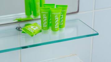 Un baño con un estante de vidrio que sostiene artículos de tocador verdes y una toalla blanca con la palabra 'boa'.