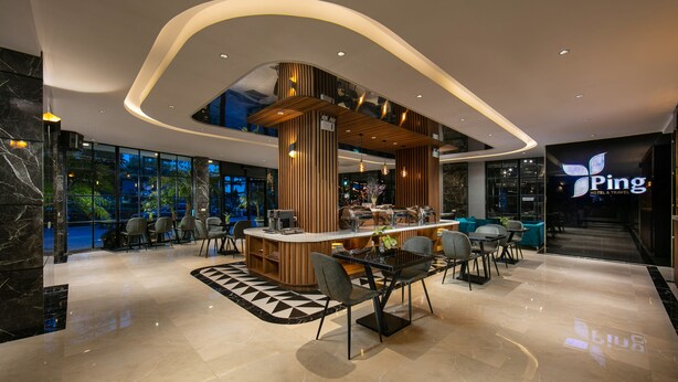 A modern hotel lobby with a central bar area, seating arrangements, and a large glass window offering a view of the outdoors. - Ping Hanoi Hotel (Hanoi)