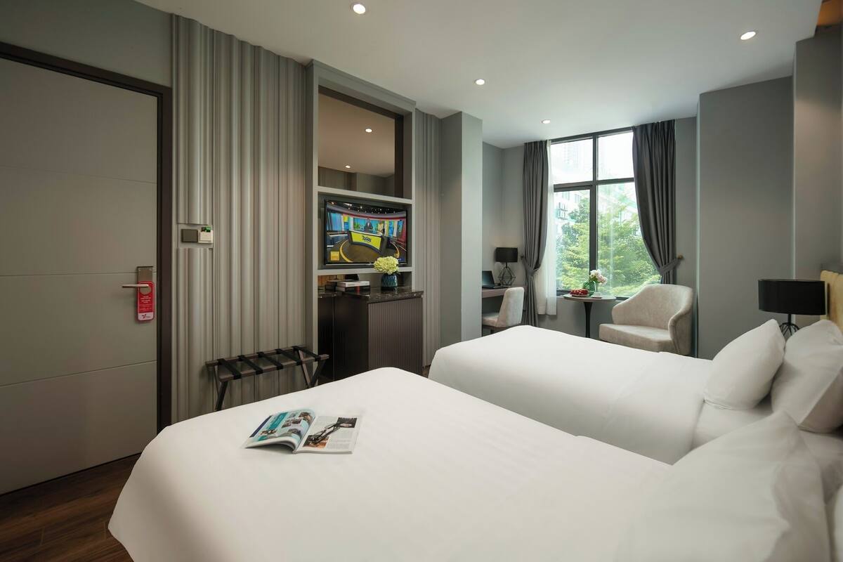 A hotel room with two beds, a desk, a chair, a TV, and a window with curtains.