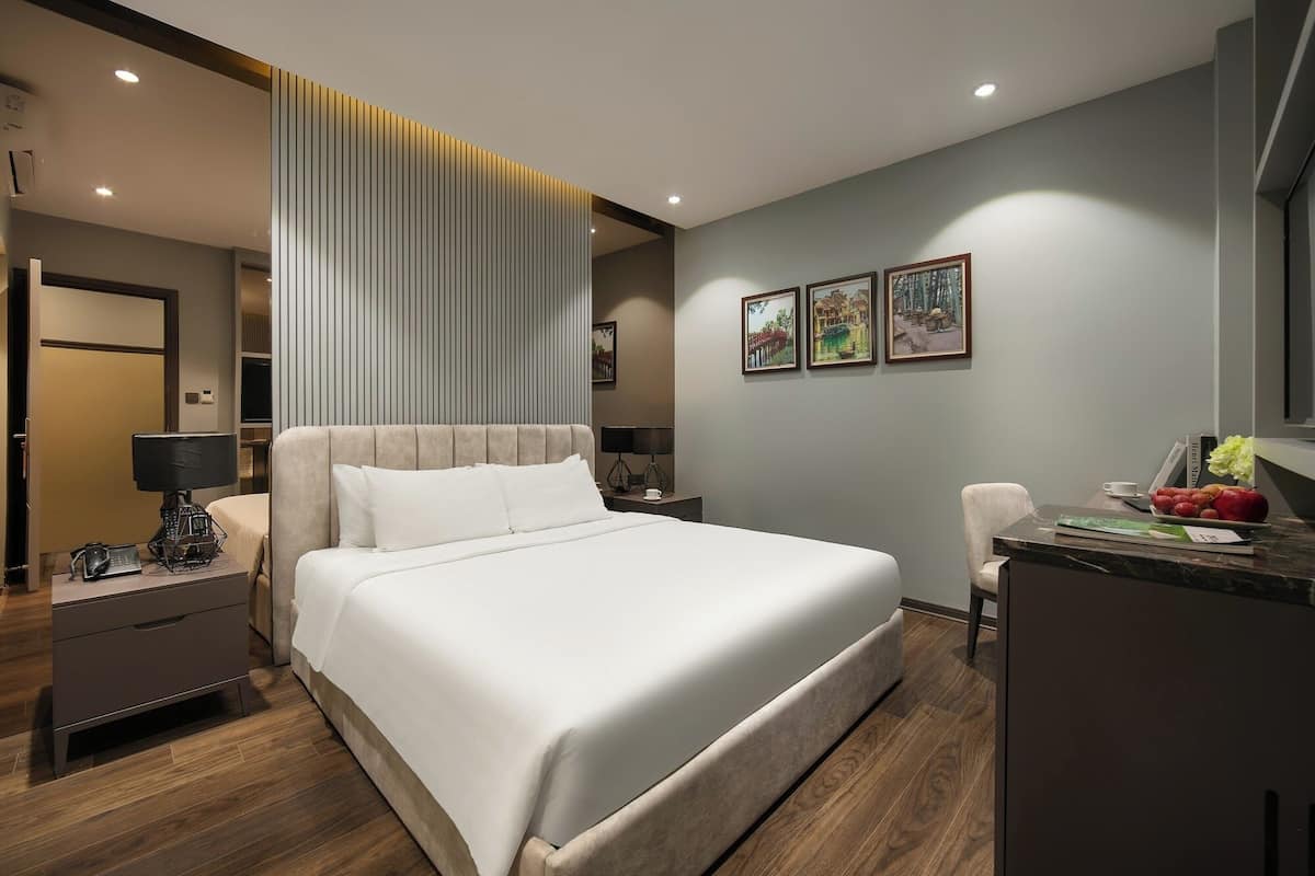 A modern hotel room with a large bed, bedside tables, a desk, and artwork on the walls.