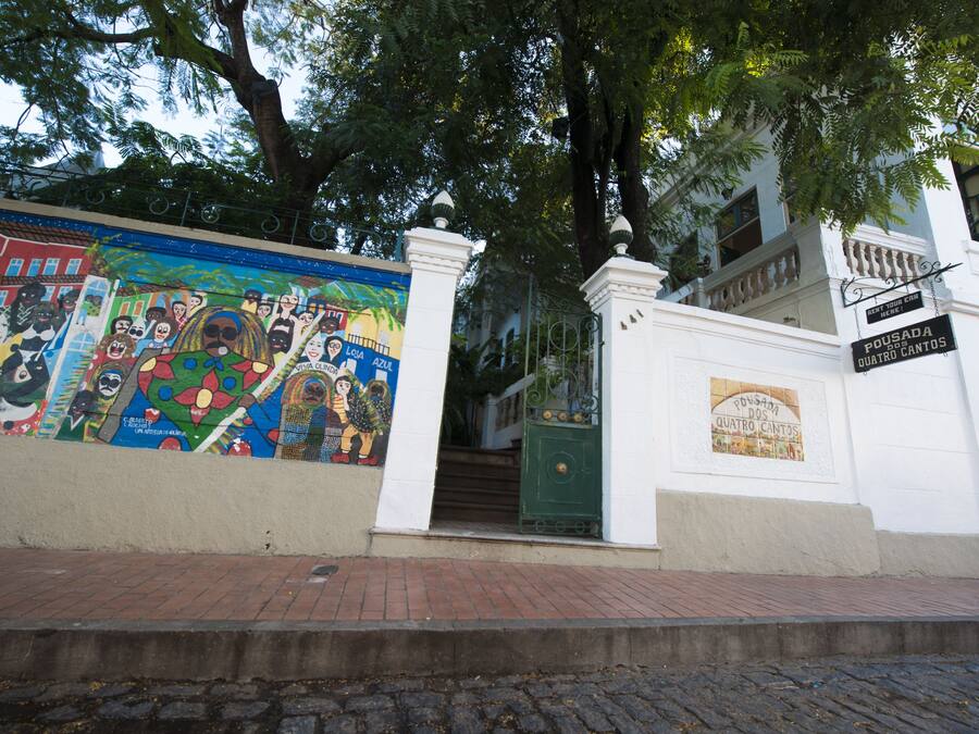 Un edificio con un mural en la pared, una verja verde y un letrero que dice "Pousada dos Quatro Cantos".