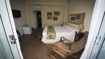 A hotel room with a bed, a wooden rocking chair, a small table, a television, and artwork on the walls.