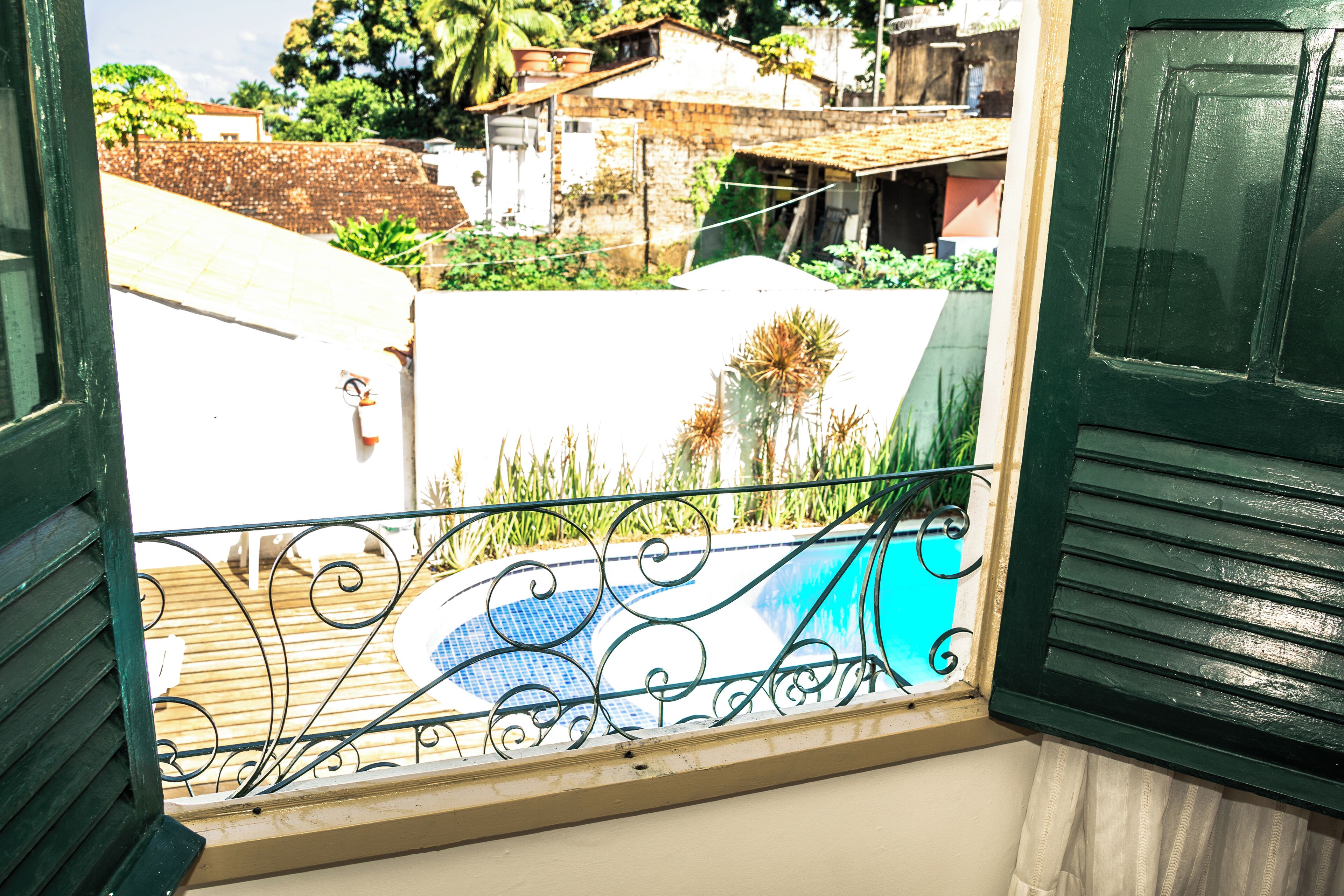 Vue depuis un balcon donnant sur une piscine, avec une rambarde en métal et un aperçu du quartier environnant.