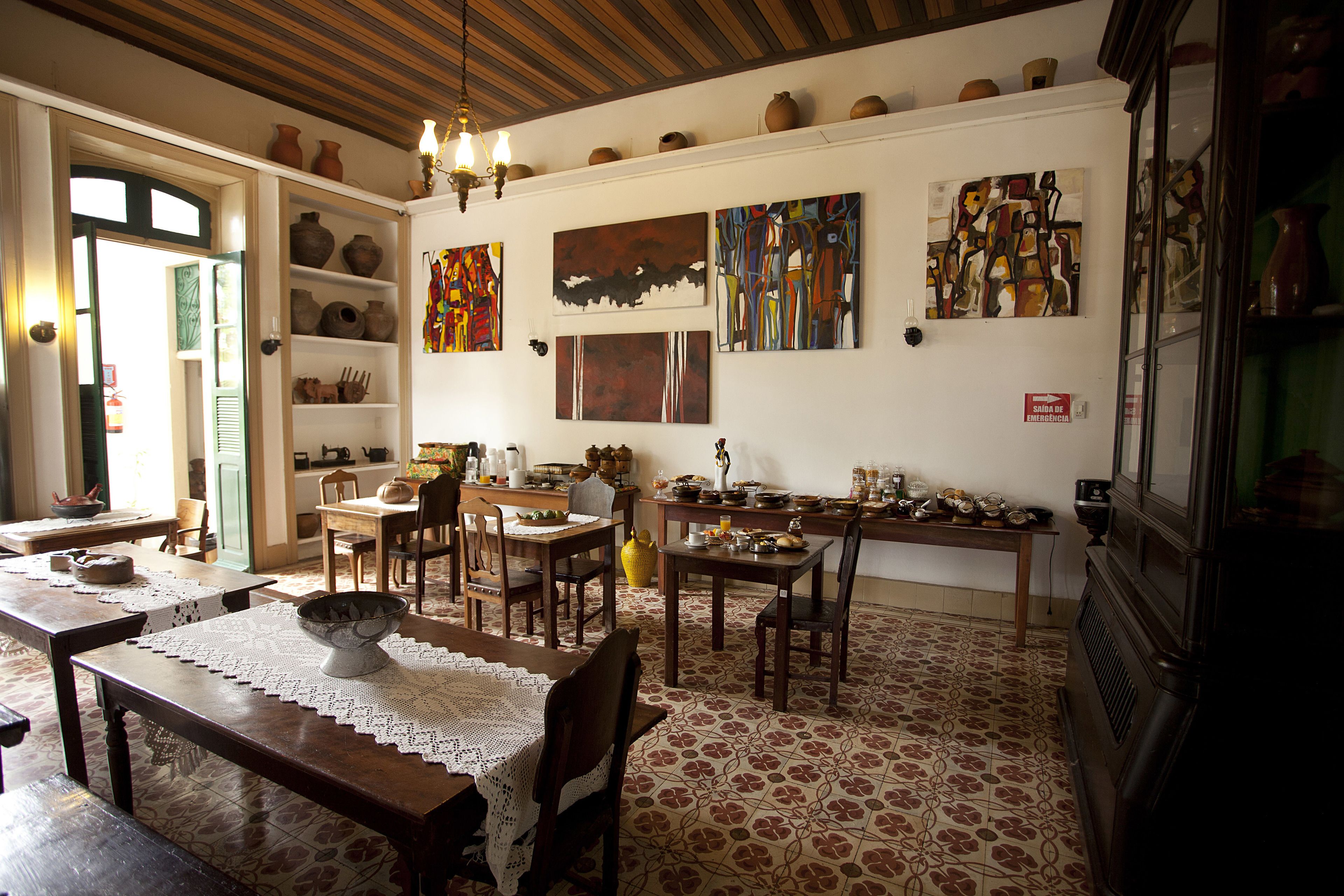 A dining area with wooden tables and chairs, a kitchen in the background, and various decorative items on the walls.
